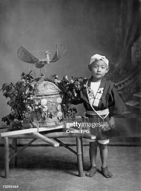 Little Japanese boy with a portable shrine topped with a stork, ready for a festival day, circa 1900.