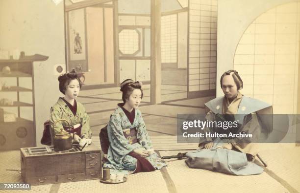 Two geishas receive a visiting samurai, Japan, circa 1880.
