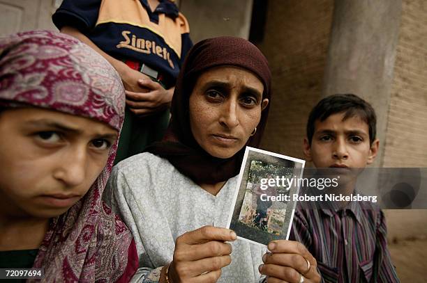 The wife of Manzoor Ahmad Mir holds a photograph of her missing husband while her children look on August 1, 2005 in Awantipora, Kashmir, India. Her...