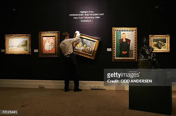 London, United Kingdom: A Sotheby's auction house porter hangs a painting entitled "Nature morte aux fruits et pot de gingembre" by Paul Cezanne...
