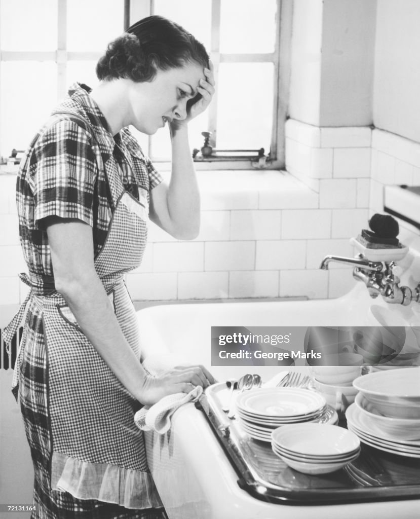 Woman suffering headache standing at kitchen sink (B&W),