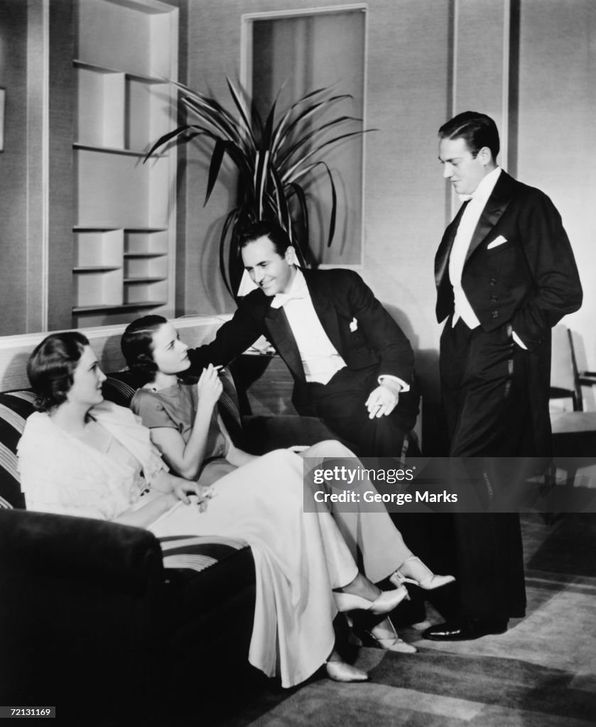 People in evening wear talking in living room (B&W)