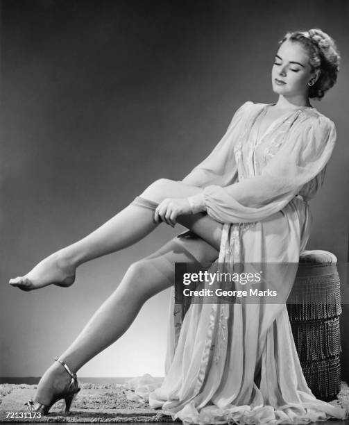 young woman putting on stockings in studio (b&w) - vintage stockings stock pictures, royalty-free photos & images