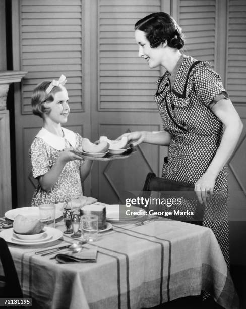 daughter (8-9) helping mother setting table for breakfast (b&w) - 1950s housewife stockfoto's en -beelden