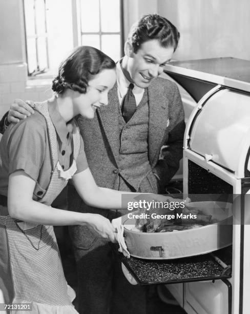 couple in kitchen, wife taking roast from oven (b&w) - stereotypical housewife bildbanksfoton och bilder