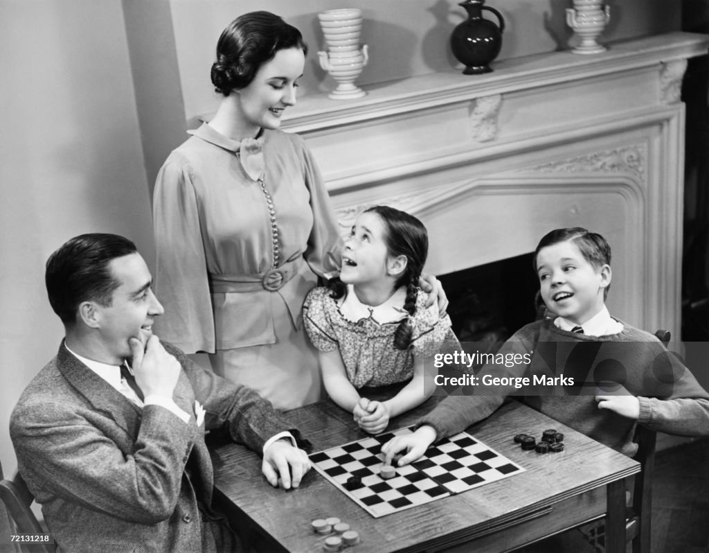 Family with two children (8-9) playing checkers (B&W), elevated view