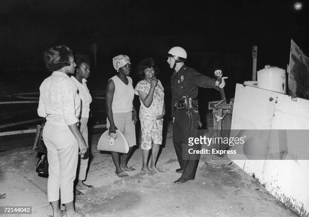 Policeman guides a group of women to safety during rioting in the Watts area of Los Angeles, August 1965. Their homes have been destroyed during the...