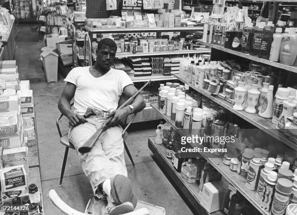 With his .22 hunting rifle on his lap and a revolver in his belt, heavyweight boxer Amos Lincoln, aka Big Train, guards the family drug store during...