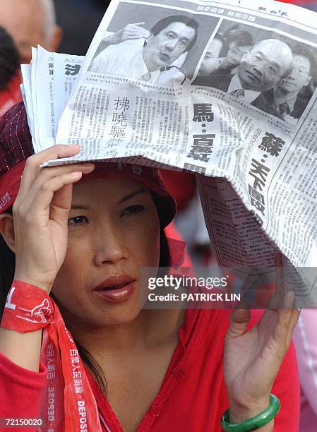 Protestor uses a copy of a newspaper carrying the images of opposition leader Taipei Mayor Ying-jeou and Premier Su Tseng-chang, to cover herself...