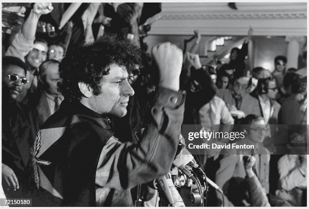 American political activist and founder of the Yippies Abbie Hoffman wears a party flag around his neck like a cape as he raises his fist in...