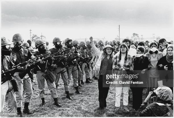 Demonstrators with locked arms pose for a photographer next to a line of armed MPs from the United States First Army, wearing gas masks and carrying...