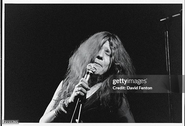 American blues-influenced rock singer Janis Joplin sings with passion into a microphone as she performs with her eyes closed on a darkened stage at...