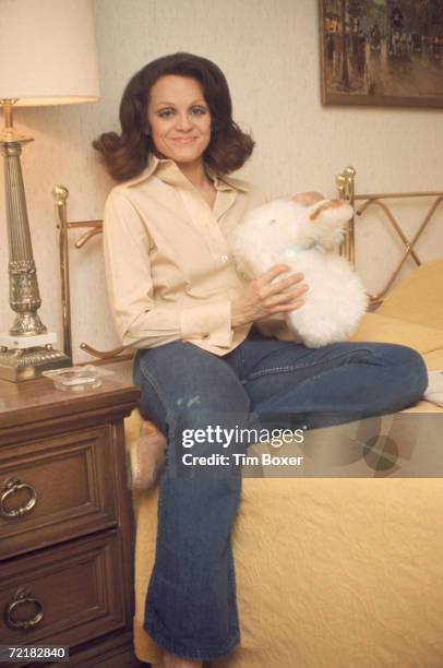 American actress Valerie Harper holds a stuffed bunny as she sits on a bed in jeans, mid 1970s.