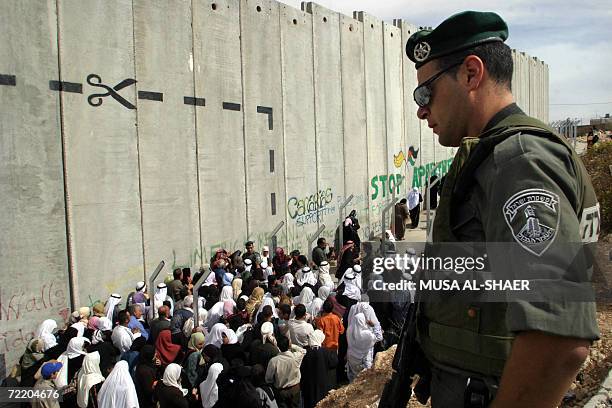 An Israeli border policeman stands guard as Palestinians gathering at a checkpoint integrated into the Israeli controversial separation barrier, on...