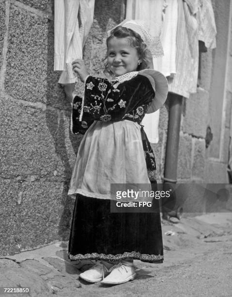 Little girl from Concarneau in Brittany takes down her parent's best linen in preparation for the Pardon of Ste Anne D'Auray, circa 1930.