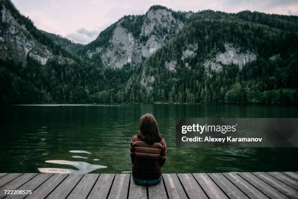 caucasian woman sitting on dock admiring scenic view of mountain - spital am pyhrn stock pictures, royalty-free photos & images
