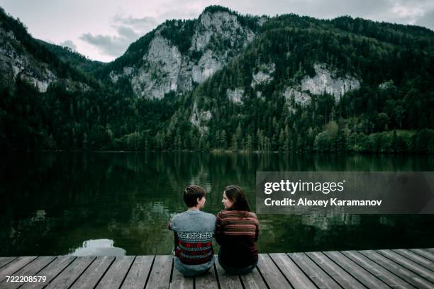 caucasian couple sitting on dock near scenic view of mountain - spital am pyhrn stock pictures, royalty-free photos & images