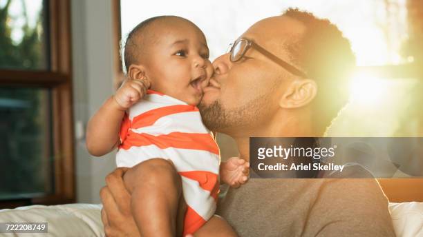 black father kissing baby son on cheek - black man holding baby stock-fotos und bilder
