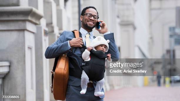 black businessman with son in baby carrier talking on cell phone - baby bag stock-fotos und bilder