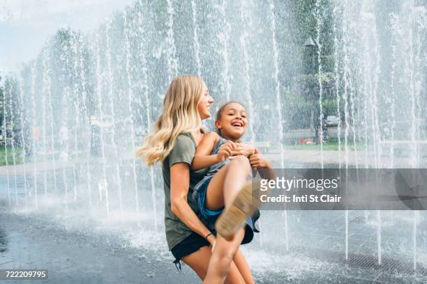 sisters playing near fountain - wasserstrahl stock-fotos und bilder