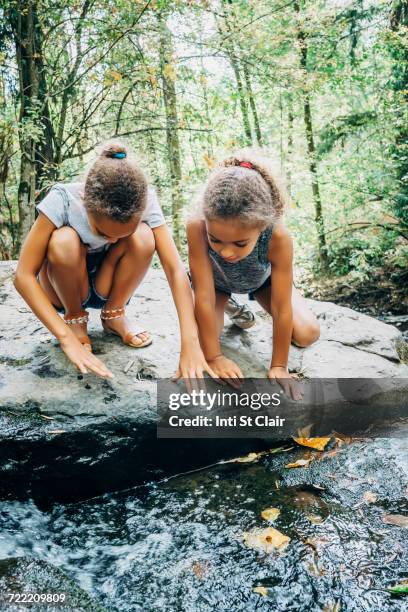 Mixed Race girls kneeling on rock looking at stream