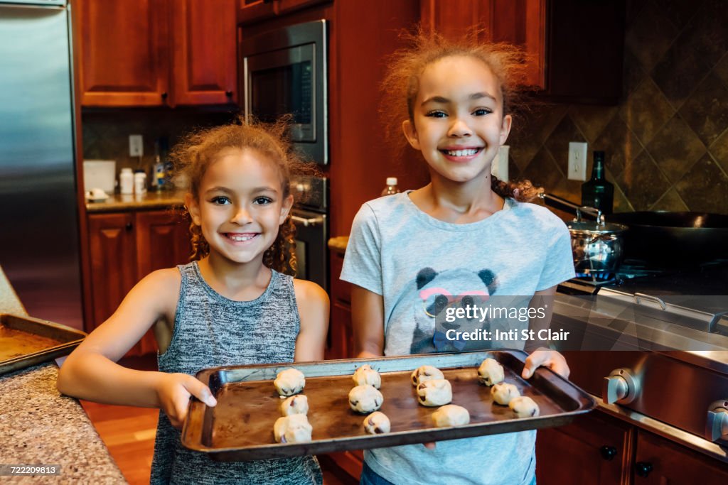 Mixed Race girls holding tray with cookie dough in domestic kitchen