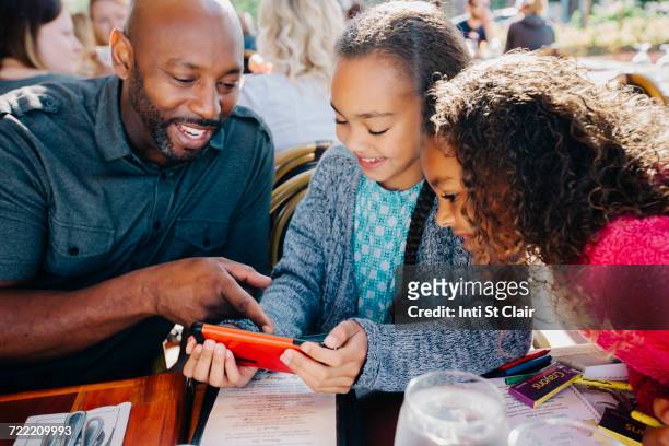 father ad daughters texting on cell phone at restaurant - african american restaurant texting stockfoto's en -beelden