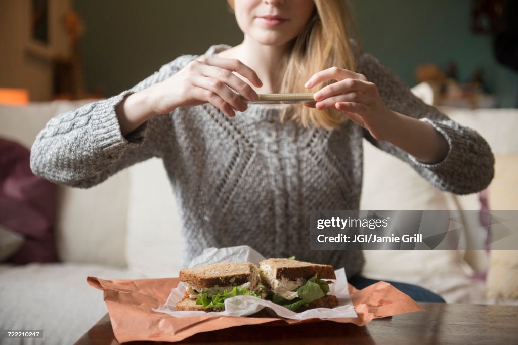 Woman photographing sandwich with cell phone