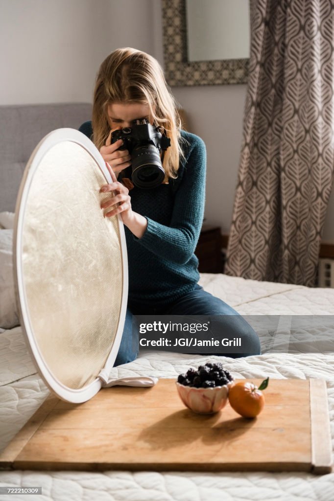 Woman kneeling on bed holding reflector photographing fruit