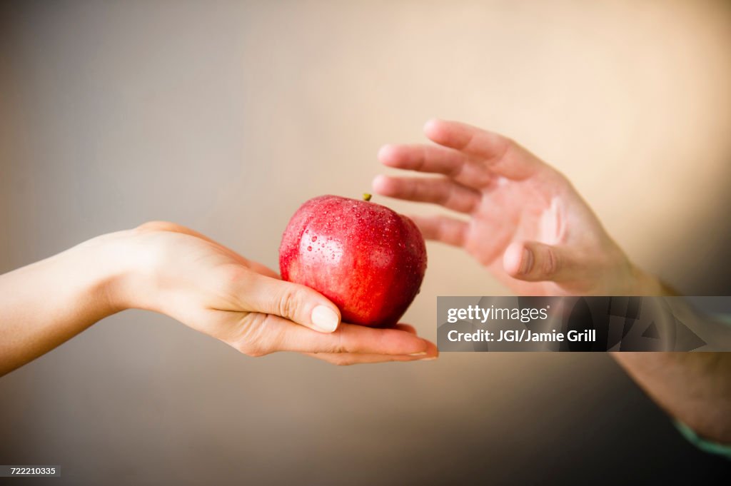 Hand of woman offering red apple to man