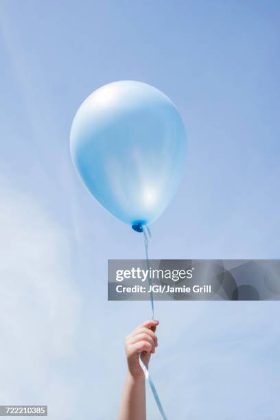 hand of caucasian girl holding blue balloon in blue sky - kid hand holding stock-fotos und bilder