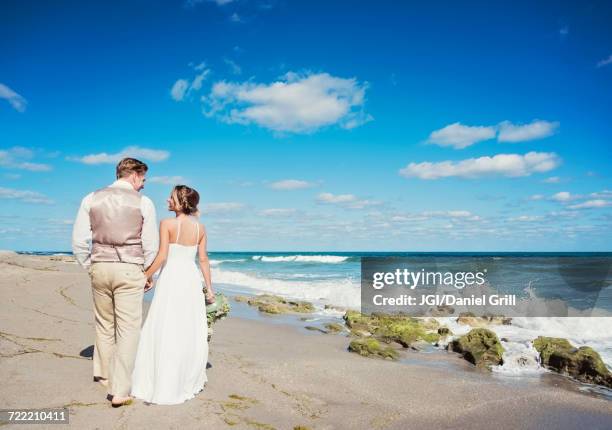 caucasian bride and groom walking on beach - destination wedding stock pictures, royalty-free photos & images
