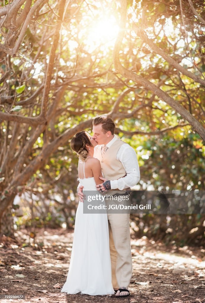 Caucasian bride and groom kissing under trees