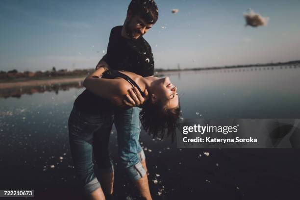 caucasian man dipping woman at lake - wet jeans stock-fotos und bilder