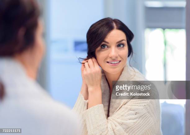 caucasian woman fastening earring in mirror - ohrring stock-fotos und bilder