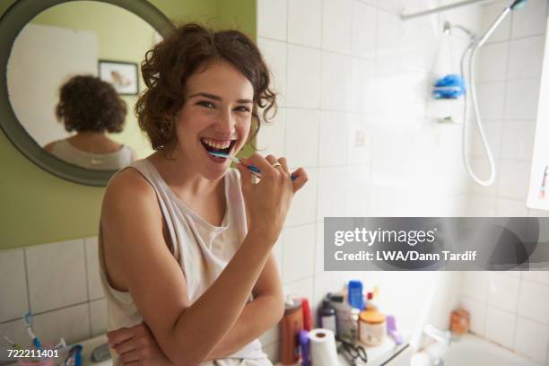 woman brushing teeth in bathroom - lavarsi i denti foto e immagini stock