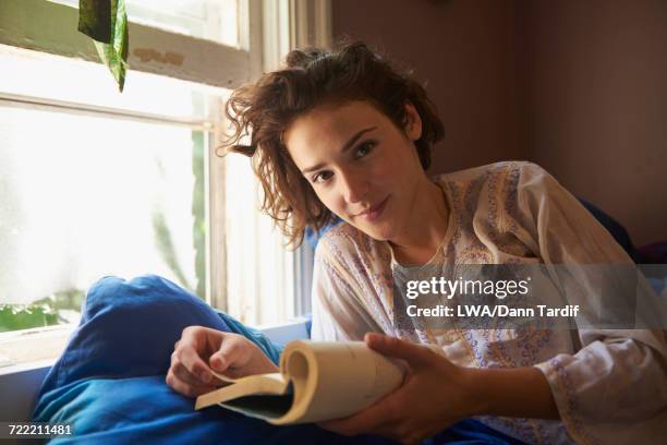 smiling woman reading book near window - lwa dann tardif bed stock pictures, royalty-free photos & images