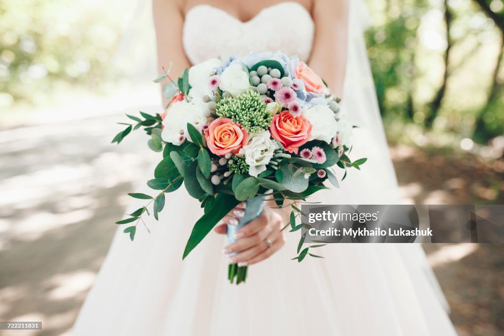Caucasian bride holding bouquet of flowers outdoors