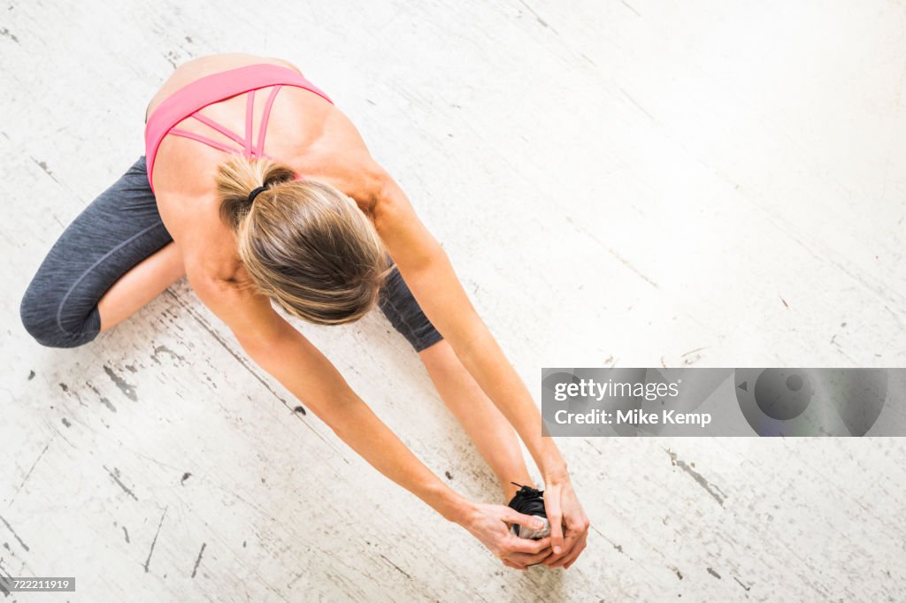 Woman sitting on wooden floor stretching leg