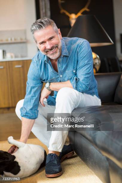 caucasian man sitting on sofa petting dog - suede shoe stock pictures, royalty-free photos & images