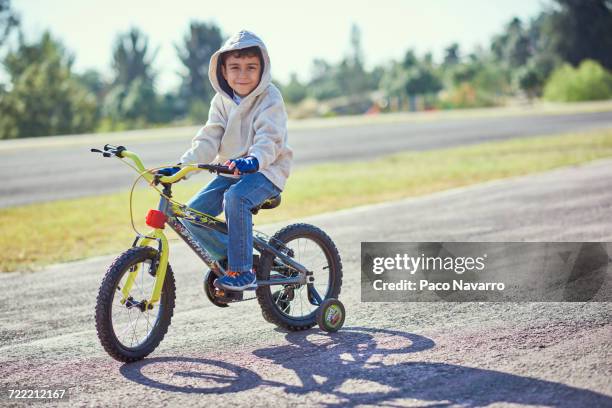 hispanic boy posing on bicycle with training wheels - training wheels stock-fotos und bilder