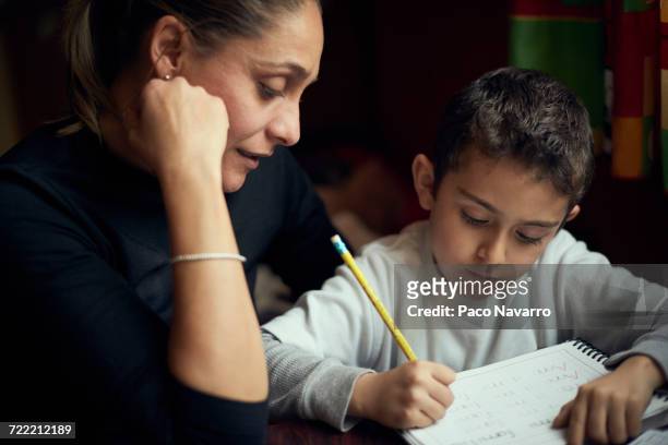 hispanic mother watching son practicing writing alphabet - mother child homework stock pictures, royalty-free photos & images