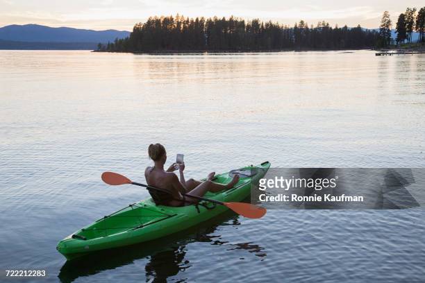 caucasian woman in kayak on river texting on cell phone - camera boat stock-fotos und bilder