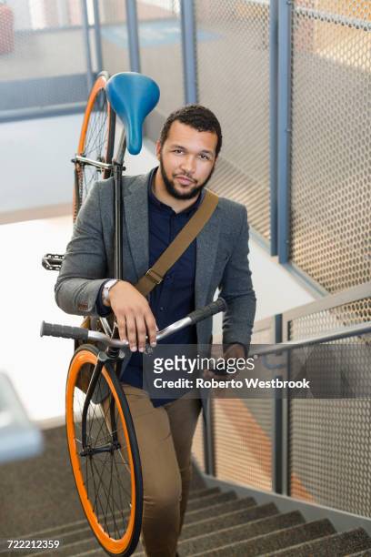 mixed race man climbing staircase carrying bicycle - borsa messenger foto e immagini stock