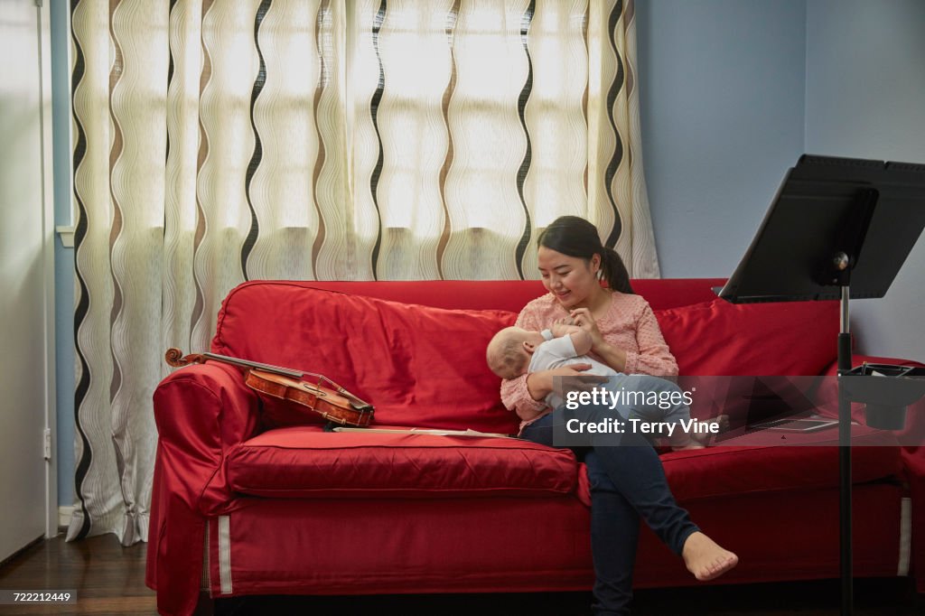 Mother feeding bottle to baby son on sofa