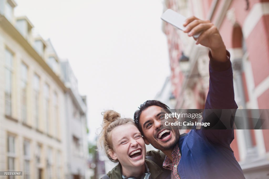 Enthusiastic, laughing young couple taking selfie in city