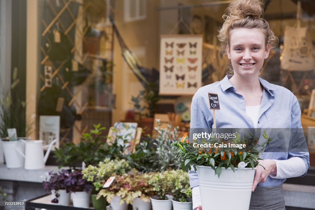 Portrait smiling female florist with potted plant at storefront