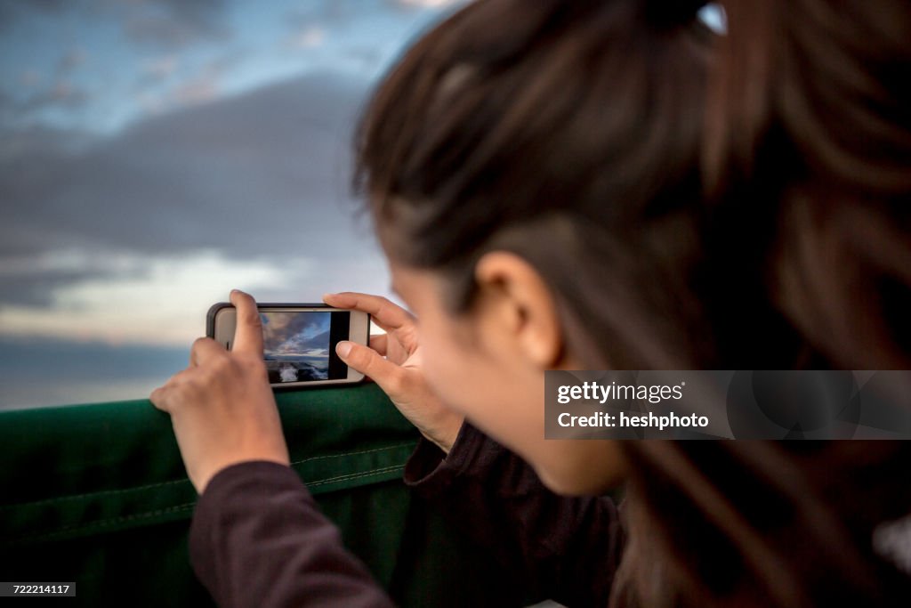 Young woman photographing sunset from boat on coast of Maine, USA