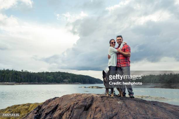 portrait of romantic mid adult couple and dog on rock at coast of maine, usa - heshphoto - fotografias e filmes do acervo