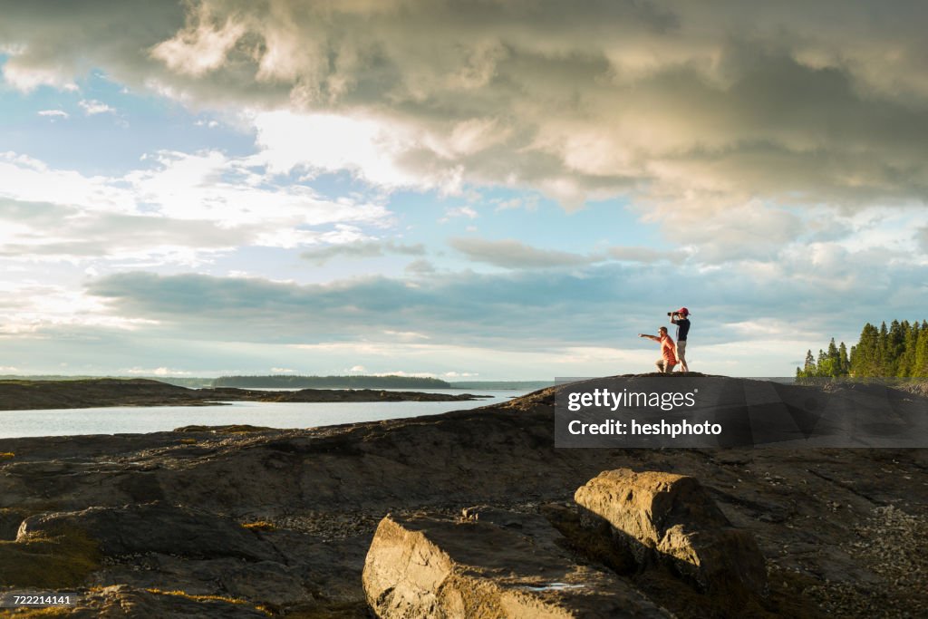 Distant view of senior man and son looking through binoculars at coast of Maine, USA